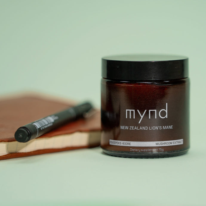 A jar of Mynd's New Zealand Lion's Mane mushroom powder placed next to a notebook and pen. 